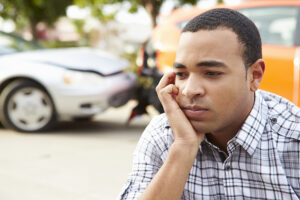 Man sitting by the side of the road looking worried after a rear end car accident